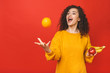 © denis_vermenko - Portrait of a smiling curly happy girl throwing orange in the air isolated over red background.