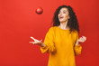 © denis_vermenko - Portrait of a smiling curly happy girl throwing apple in the air isolated over red background.
