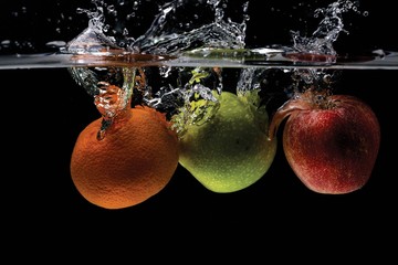 Close up view of colorful fruits falling in water on black background.  Gorgeous backgrounds.