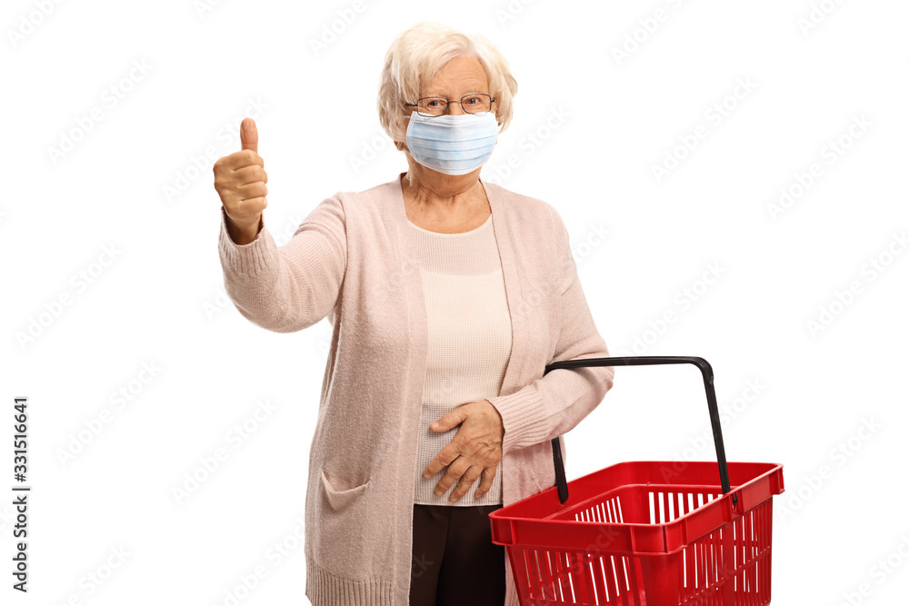 Elderly woman wearing a face medical mask showing a thumb up sign and holding a shopping basket - obrazy, fototapety, plakaty 
