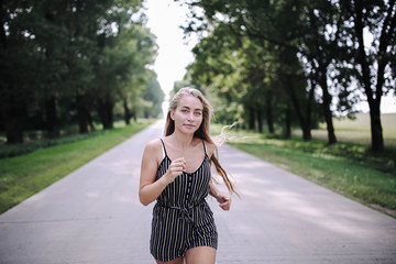 young long-haired girl runs on a summer road  the trees, the concept of a joyful morning.