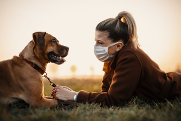 Woman wearing a protective mask is walking alone with a dog outdoors because of the corona virus pandemic covid-19