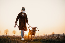 Woman Wearing A Protective Mask Is Walking Alone With A Dog Outdoors Because Of The Corona Virus Pandemic Covid-19