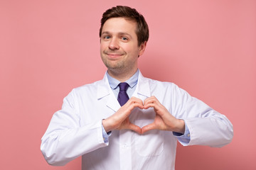 Wall Mural - Smiling caucasian medical male doctor showing heart figure with fingers