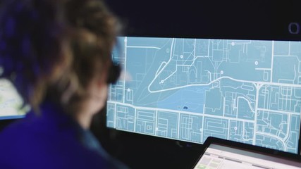 Close on female emergency dispatcher with headset, rack focus to map on screen