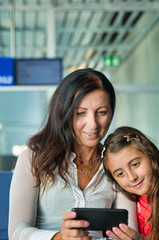 Sticker - Mother and daughter at the airport reviewing holiday images taken with smartphone