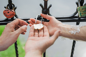 Bride ang groom holding golden heart lock with key. Love symbol. Romantic vacation. Valentine day, wedding, relationship concept. Padlocks hanging on bridge. Russian tradition