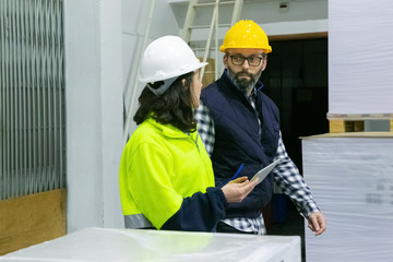 Two factory workers walking with tablet at plant. Confident machine operators talking while walking at factory. Print manufacturing concept