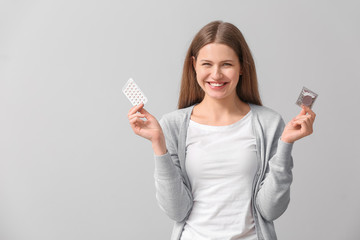 Sticker - Young woman with birth control pills and condom on grey background