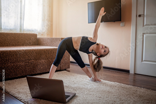 Fotografía Pretty young girl in sportswear watching online video on laptop and doing fitnes
