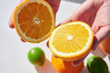 Wall Mural - Ripe orange halves in woman’s hands, shot from above in harsh sunlight. Fruits on background.