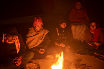 A cheerful Indian Bengali brunette family in winter wear enjoying bonfire  on rooftop in the evening. Indian lifestyle and winter.