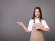 © LumenSt - Young woman in an apron on a gray background.