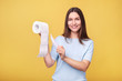 © LumenSt - Young woman holds toilet paper on  yellow background.