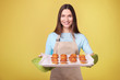 © LumenSt - Young woman in apron with cupcakes on a yellow background