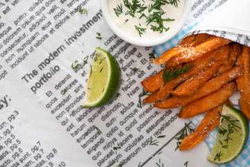 top view of crispy french fries, sliced lime and garlic sauce on newspaper