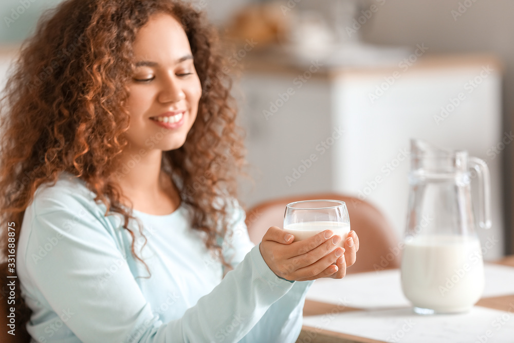 Young African-American woman with milk in kitchen
