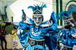 man in variegated blue costume poses for photo on city street at dominican carnival