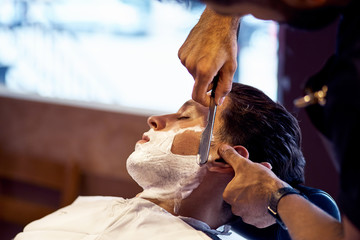 Shaving process of beards in Barbershop. Master makes the client shave his beard with vintage straight razor.