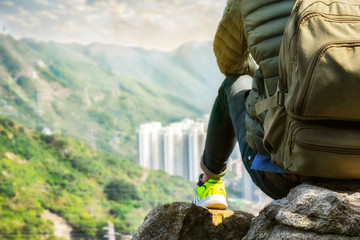 A young traveler man sitting on the top of mountain with a  bag pack and enjoy the beauty of city view. travel concept