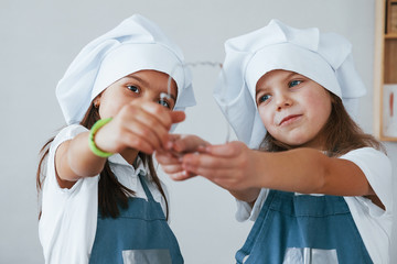 Two little girls in blue chef uniform working with flour on the kitchen