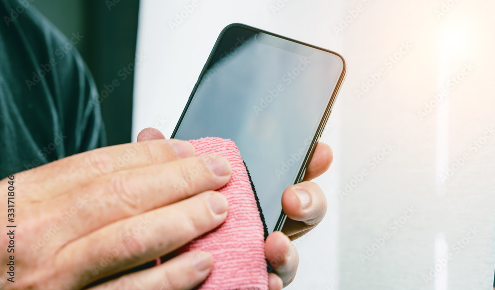 Person Cleaning mobile phone screen with disinfecting wipes for clean smartphone. COVID-19 Coronavirus outbreak contamination prevention concept. - obrazy, fototapety, plakaty 