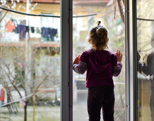 The child alone stands on the windowsill. Baby safety at home. Cute girl looks out the open window.