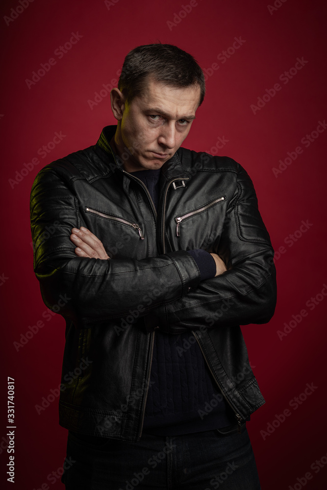 Brutal man in a black leather jacket poses against a dark red ...