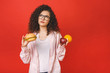 © denis_vermenko - Attractive young student woman makes a choice between healthy and unhealthy foods, apple and hamburger isolated on red background.