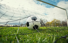 Close Up Of A Soccer Ball Enters The Gate And Hits The Net, Goal Concept. Football Championship Background, Spring Outdoors Tournaments. Healthy Sports Activity And Games.