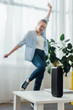 © LIGHTFIELD STUDIOS - Selective focus of portable speaker and laptop on coffee table and cheerful woman dancing in living room