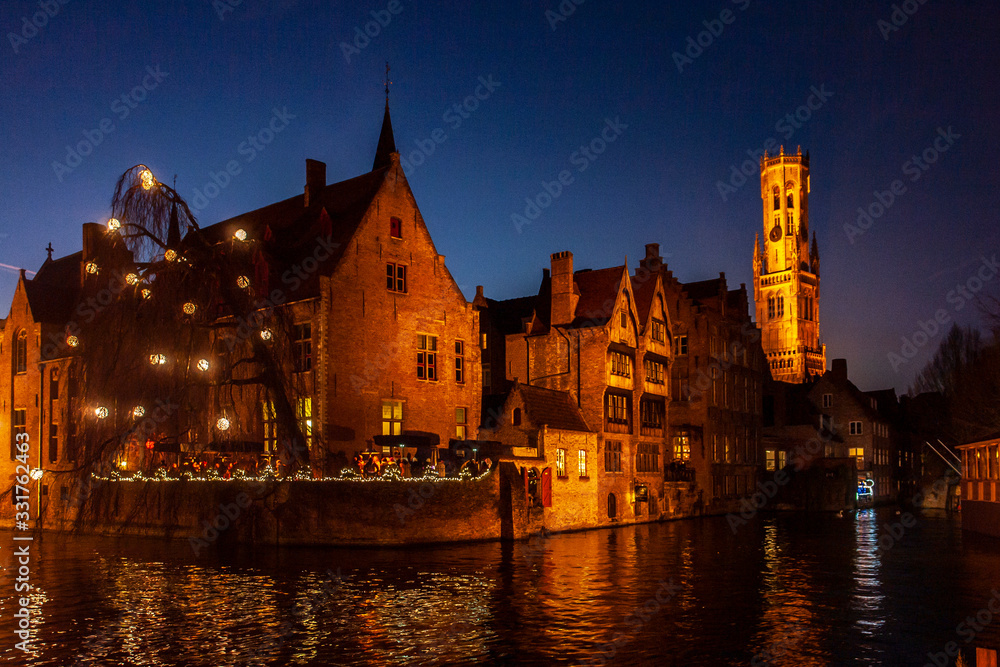 Brujas de noche con una de sus torres medievales y un canal en primer plano - obrazy, fototapety, plakaty 