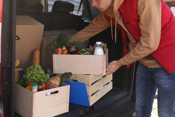 Courier taking crate with products from car, closeup. Food delivery service