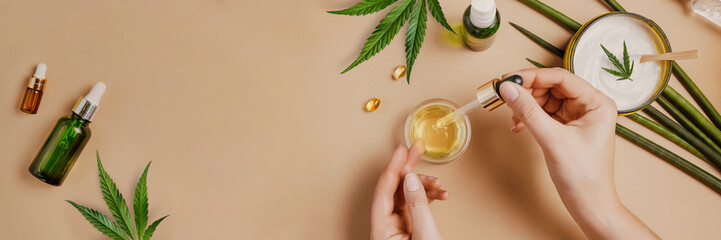 pipette with cbd cosmetic oil in female hands on a table background with cosmetics, cream with canna