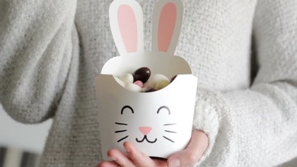 Wall Mural - Woman holding a treat box in shape of bunny and eating easter almonds from it