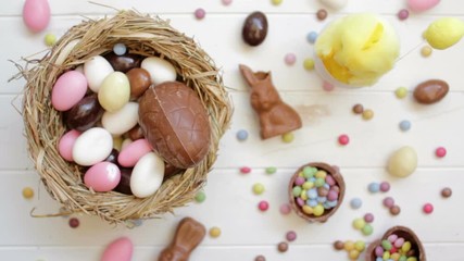 Wall Mural - Hands taking almonds and chocolate eggs from table decorated with Easter candy. Top view