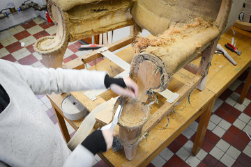 Wall Mural - Making new upholstery on old chair. Armchair upholstery in upholstery workshop. Working with hand tools. Stretching new straps on seat. Woman working. Scissors cutting. 