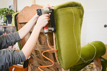 Making new upholstery on old restored furniture. Woman work with pneumatic stapler in upholstery workshop.  Green velvet fabric.