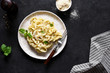 Tagliatelle pasta with cheese sauce and basil in a plate on the kitchen table.