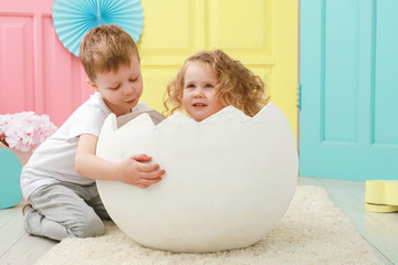 Older brother take care about his little sister is sitting in a white egg that hatched against a studio colorful background. Famly concept.