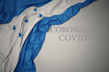 waving national flag of honduras on a gray background with text coronavirus covid-19 . concept.