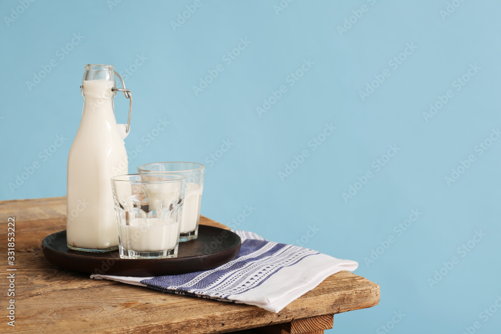 Glassware with fresh milk on table against color background