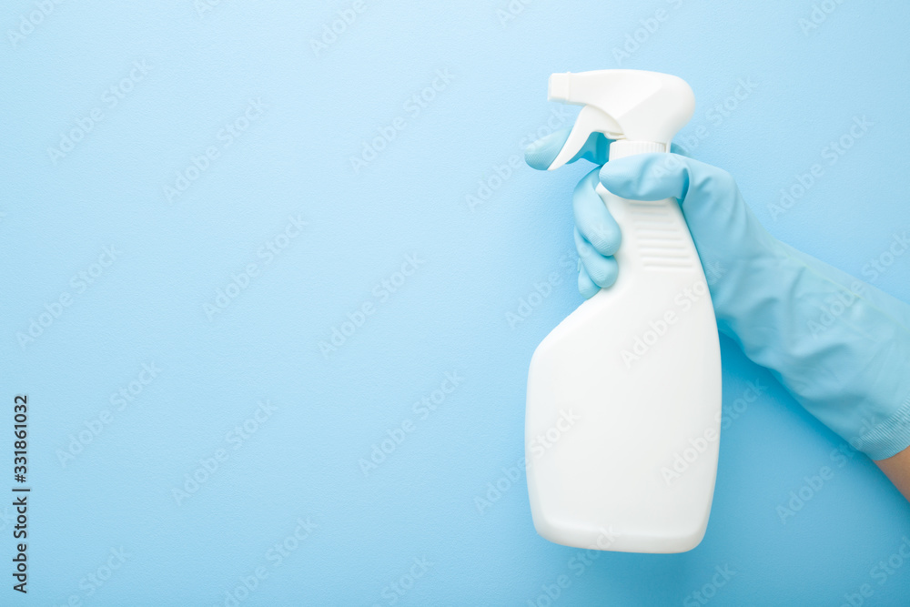 Hand in rubber protective glove holding white spray bottle. Detergent for different surfaces in kitchen, bathroom and other rooms. Closeup. Empty place for text or logo. Light pastel blue background. - obrazy, fototapety, plakaty 