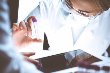 Wall Mural - Coronavirus pandemic. Professional female scientist in protective eyeglasses researching tube with reagents in laboratory. Concepts of medicine and virus protection