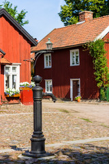 Wall Mural - Old water pump in a square with idyllic Swedish red cottages