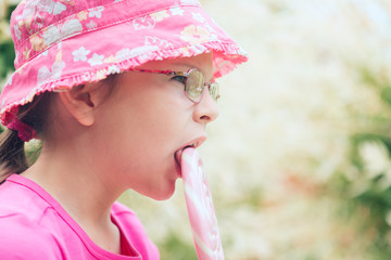 Little girl in a pink hat licking big lollipop