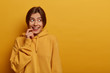 © WHstudio Leushin N - Positive good looking woman has nice idea, looks mysteriously aside, smiles gently, wears casual sweatshirt, makes up plan, has combed dark hair, isolated on yellow background, empty space right