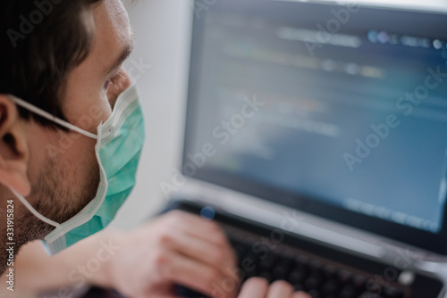 Remote work in quarantine. Compliance with all safety rules. Wear a mask everywhere. The programmer writes code on a laptop.