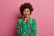 © wayhome.studio - People, happy emotions and feelings concept. Joyful dark skinned young woman keeps hand under chin, looks tenderly at camera, has hilarious conversation, wears green jumper and overalls, models indoor