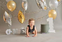 Smash Cake Party. Little Cheerful Birthday Boy With First Cake. Happy Infant Baby Celebrating His First Birthday. Decoration And Photo Zone For First Year. One Year Baby Celebration. Grey Decor.